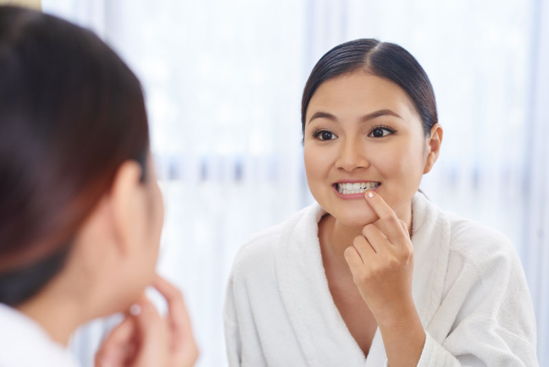 woman looking at teeth in mirror